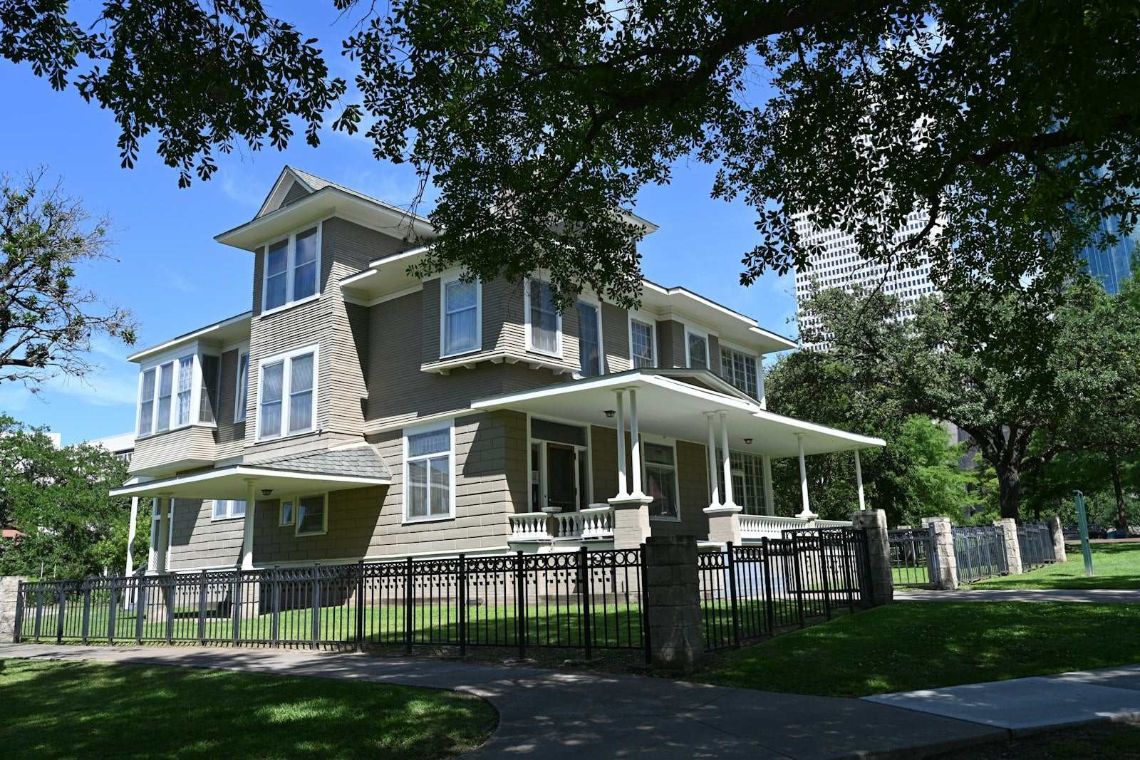Two-story house with a porch behind a fence and trees
